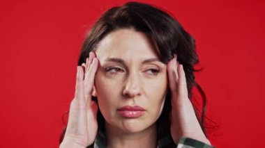 Acı çeken güzel bir kadının portresi baş ağrısı, kırmızı stüdyo portresi. Kadın ellerini başının üstüne koyuyor. Migren sorunları, ilaç, hipertansiyon, manyetik fırtınalar kavramı. 4k