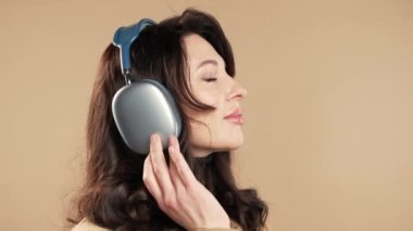 Mutlu iş kadını kafayı bulur, müzik dinler, bej renkli stüdyo arka planında kulaklıklarla dans etmekten zevk alır. Radyo, kablosuz modern ses teknolojisi, çevrimiçi çalar. Yüksek kalite 4k