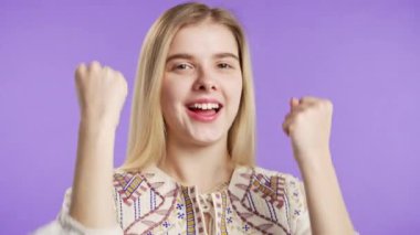 Güzel bir genç kadın zafer işareti gösterir. Zafer, başarılar, hedefler. Mutlu, mutlu, şaşırmış, mor arka plandaki mutlu bayan. Büyük ikramiye konsepti. Yüksek kalite 4k