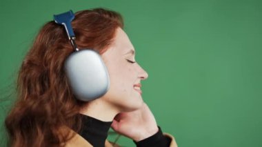 Mutlu kadın kafayı bulur, müzik dinler, yeşil stüdyo arka planında kulaklıklarla dans etmekten zevk alır. Radyo, kablosuz modern ses teknolojisi, çevrimiçi çalar. Yüksek kalite 4k