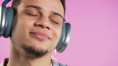 Müzik dinleyen pozitif çok ırklı bir adam, pembe stüdyo arka planında modern kulaklıklarla dansın tadını çıkarıyor. Radyo, kablosuz modern ses teknolojisi, çevrimiçi çalar. Yüksek kalite 4k