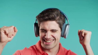 Pozitif beyaz Avrupalı adam müzik dinliyor, mavi stüdyo arka planında modern kulaklıklarla dans ediyor. Radyo, kablosuz modern ses teknolojisi, çevrimiçi çalar. Yüksek kalite 4k