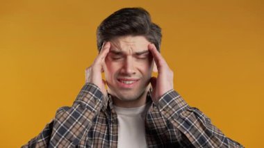 Baş ağrısı çeken genç bir adam, stüdyo portresi. Adam ellerini başının üstüne koyuyor, sarı arka planda izole edilmiş. Sorunlar, ilaç, hastalık kavramı