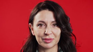 Oldukça olgun bir Avrupalı kadın göz kırpıyor, flört ediyor ve kameraya gülümsüyor. Stüdyoda kırmızı arka planda bir bayan. Yüksek kalite 4k görüntü