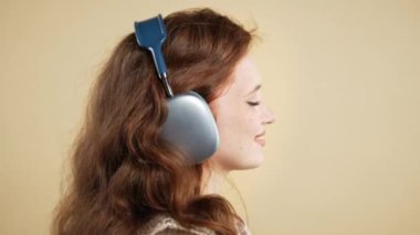 Mutlu kadın kafayı bulur, müzik dinler, bej renkli stüdyo arka planında kulaklıklarla dans etmekten zevk alır. Radyo, kablosuz modern ses teknolojisi, çevrimiçi çalar. Yüksek kalite 4k