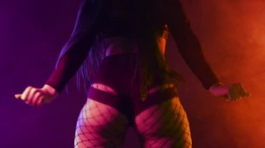 Dans eden, titreyen, külotlu çorap giyen, çok renkli ışığın altında kıvrımlı kalçalı, karanlık stüdyo arka planı olan seksi bir kadın. Modern dans, twerk. Yüksek kalite 4k görüntü