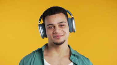 Müzik dinleyen olumlu bir adam, sarı stüdyo arka planında modern kulaklıklarla dansın tadını çıkarıyor. Radyo, kablosuz modern ses teknolojisi, çevrimiçi çalar. Yüksek kalite 4k