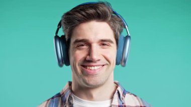 Müzik dinleyen olumlu bir adam, mavi stüdyo arka planında modern kulaklıklarla dansın tadını çıkarıyor. Radyo, kablosuz modern ses teknolojisi, çevrimiçi çalar. Yüksek kalite 4k