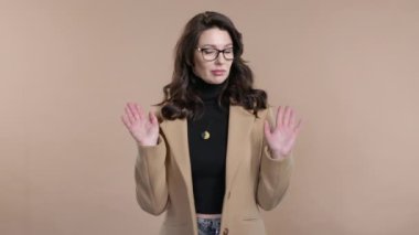 Kafası oldukça karışık bir iş kadını, omuzları kalkık, yardımcı olamıyor, bir jest yapıyor. Zor soru, suçlu tepkisi, bej arka planda şaşkın stil sahibi bir kadın. Yüksek kalite 4k