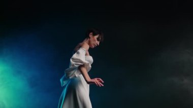 Lüks beyaz elbiseli nazik, kadınsı bir kadın. Karanlık stüdyoda dans eden kadın kol koreografisi tarzı dans ediyor. Yüksek kalite 4k görüntü