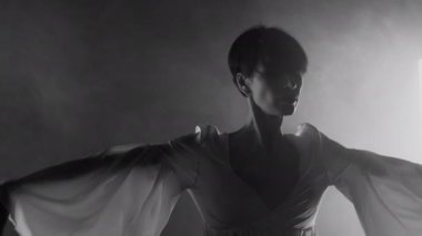 İpek elbiseli muhteşem kadın modern koreografi sergiliyor. Siyah beyaz stüdyoda kollarıyla çağdaş stil dansı yapıyor. Yüksek kalite 4k görüntü