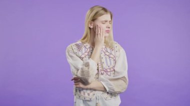Violet stüdyosunun arka planında diş ağrısı olan güzel bir kadın. Diş ağrısı, diş sorunları, diş hekimliği ve ilaç konsepti. 4k