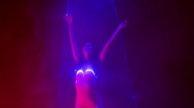 Pembe ışık altında dans eden seksi elbiseli muhteşem kadın, lazer ışığı, neon duman kulübü. Projeksiyon illüzyon haritası. Fütürist model. Yüksek kalite 4k