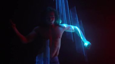 Uzun saçlı, çıplak vücutlu yakışıklı bir adam. Çıplak karın kasları, parlak ışık altında dans eden eller, lazer ışığı, neon duman kulübü. Projeksiyon illüzyon haritası. Fütürist model.