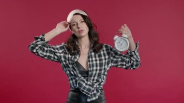 Alarmlı saatle uyandı uykulu, 40 'lı yaşlarda elinde tutan bir kadın. Kırmızı arka plan. Sabahın 9 'unda. Tembel adam yeterince uyuyamadı, zaman geçirme kavramı. Yüksek kalite 4k