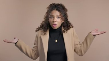 Kafası karışık, afro-amerikan bir kadın, omuzları yukarıda, yardımcı olamıyor, bilmiyorum jestler yapıyor. Zor soru, suçlu tepkisi, bej arka planda şaşkın stil sahibi bayan. Yüksek kalite 4k