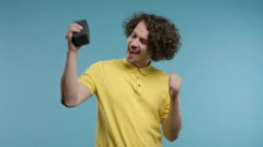 Dans eden adam, mavi stüdyo arka planında eğleniyor. Adam müziğin ritmine göre hareket ediyor. Genç adam kablosuz taşınabilir hoparlörden müzik dinliyor. Modern ses sistemi. Yüksek kalite 4k