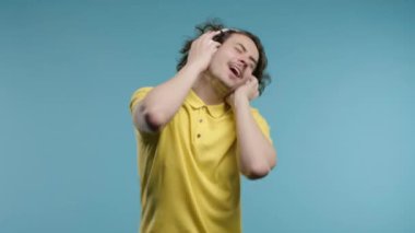 Müzik dinleyen olumlu bir adam, mavi stüdyo arka planında modern kulaklıklarla dansın tadını çıkarıyor. Radyo, kablosuz modern ses teknolojisi, çevrimiçi çalar. Yüksek kalite 4k