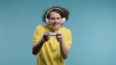 Televizyonda video oyunu oynayan yakışıklı genç adam mavi stüdyo arka planında joystick izole edilmiş. Modern teknolojiyi kullanarak.