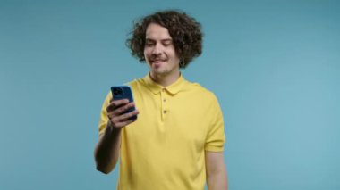 Akıllı telefondan internette sörf yapan yakışıklı bir erkek. Mavi arka planda gülücük ve neşe dolu bir adam. Teknoloji, başarı, mutluluk, sosyal ağ konsepti. Yüksek kalite 4k