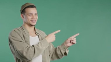 Gülümseyen genç adam reklamınız için boş bir yer arıyor. Sağ tarafı gösteren adam öneriliyor, boşluğu kopyalayın. Erkek model yeşil arka planda izole edilmiş bir şey sunuyor. Yüksek kalite 4K görüntü.