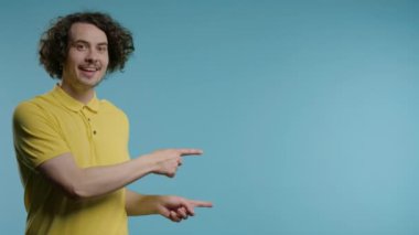 Gülümseyen genç adam reklamınız için boş bir yer arıyor. Sağ tarafı gösteren adam öneriliyor, boşluğu kopyalayın. Erkek model mavi arka planda izole edilmiş bir şey sunuyor. Yüksek kalite 4K görüntü.