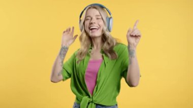 Mutlu kadın kafayı bulur, müzik dinler, sarı stüdyo arka planında kulaklıklarla dans etmekten zevk alır. Radyo, kablosuz modern ses teknolojisi, çevrimiçi çalar. Yüksek kalite 4k