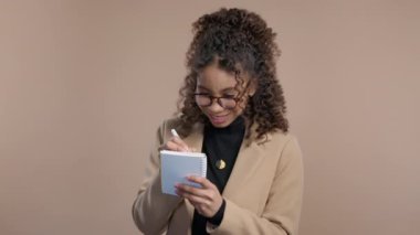 Genç kız kalemle planlamacıyla notlar yazıyor. Afrikalı kadın gelecek planları ve yapılacaklar listesini haftalar, aylar, yıllar boyunca not defterinde düşünüyor. Bej arka planda kişisel günlük tutuyorum. 4k