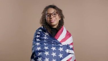 Bej arka planda ulusal bayrağı olan gülümseyen Afrikalı Amerikalı kadın. Amerikan vatansever, 4 Temmuz Bağımsızlık Günü kutlamaları, seçimler, Amerika, işçiler. Amerikan bayrağı. Yüksek kalite 4k