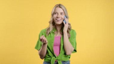 Telefonda konuşan çekici bir kadın, hoş bir şaka, gülümsüyor. Sarı arka plandaki genç bayan. Akıllı telefon görüşmesi. - Evet. Yüksek kalite 4k