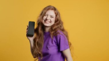 Dans eden bir kadın, sarı stüdyo arka planında eğleniyor. Kız müziğin ritmine göre hareket ediyor. Kablosuz taşınabilir hoparlörden müzik dinleyen genç - modern ses sistemi.