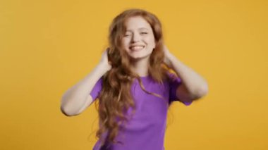 Komik, 20 'li yaşlarda güzel bir kadın eğleniyor, en sevdiği müzik çalıyor, gülümsüyor, sarı stüdyo arka planında dans ediyor. Müzik, dans konsepti, 4k