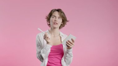 Kalemle not yazan genç bir kadın. Bayan gelecek planları ve yapılacaklar listesini haftalar, aylar, yıllar boyunca not defterinde düşünüyor. Kişisel günlüğümü pembe arka planda tutuyorum. 4k