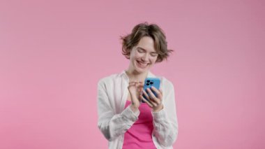Akıllı telefondan internette sörf yapan güzel bir kadın. Pembe arka planda gülücük ve neşe dolu bir kız. Teknoloji, başarı, mutluluk, sosyal ağ konsepti. Yüksek kalite 4k