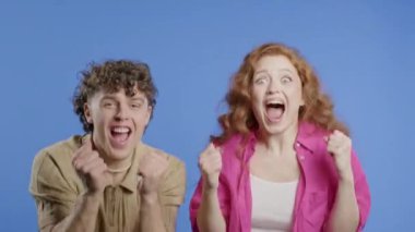 Güzel kadın ve erkek zaferlerini gösteriyor. Zafer jestleri, başarılar, hedefler. Mor arka planda mutlu, mutlu ve şaşırmış şık bir çift. Büyük ikramiye konsepti. Yüksek kalite 4k