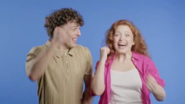 Güzel kadın ve erkek zaferlerini gösteriyor. Zafer jestleri, başarılar, hedefler. Mor arka planda mutlu, mutlu ve şaşırmış şık bir çift. Büyük ikramiye konsepti. Yüksek kalite 4k