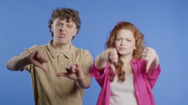 Mutsuz Avrupalı kadın ve erkeğin portresi, hoşlanmama işaretiyle kınanıyor. Violet stüdyosunun arka planında olumsuz jest yapan bir çift..