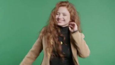 Komik, güzel, 20 'li yaşlardaki öğrenci kadın eğleniyor, en sevdiği müzik, gülümsüyor, yeşil stüdyo arka planında dans ediyor. Müzik, dans konsepti, 4k
