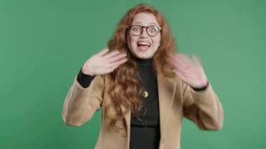 Dost canlısı genç iş kadını el sallıyor. Merhaba, ya da hoşça kal, kaos, adios. Ayrılıyorum, kameraya hoşça kal de. Yeşil stüdyo geçmişinde güzel bir bayan öğrenci. Yüksek kalite 4k görüntü