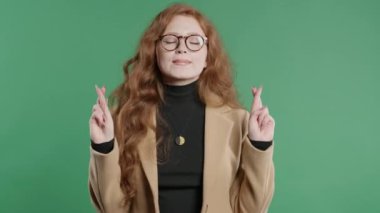 Yeşil arka planda dua eden güzel, genç, kızıl bir kız öğrenci. Hanımefendi birine arzularını tatmin etmesi için yalvarır, yardım eder, şans için dua eder. Yüksek kalite 4k