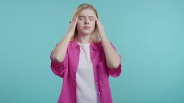 Güzel, acı çeken genç bir kadının portresi baş ağrısı, mavi bir stüdyo portresi. Kadın ellerini başının üstüne koyuyor. Migren sorunları, ilaç, hastalık, manyetik fırtınalar kavramı. 4k