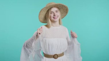 Bohem tarzı elbise ve hasır şapkalı komik genç nesil kız eğleniyor, en sevdiği müzik, gülümsüyor, mavi stüdyo arka planında dans ediyor. Müzik, dans konsepti, 4k