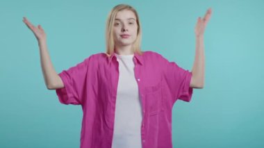 Kafası karışık bir kadın, omuzları yukarıda. Yardımcı olamıyor. Bilmiyorum. Zor soru, suçlu tepkisi, şaşkın genç kız mavi arka planda. Yüksek kalite 4k