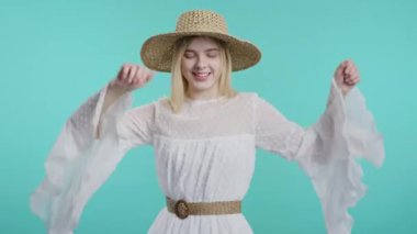 Bohem tarzı elbise ve hasır şapkalı komik genç nesil kız eğleniyor, en sevdiği müzik, gülümsüyor, mavi stüdyo arka planında dans ediyor. Müzik, dans konsepti, 4k