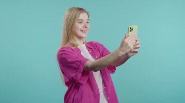 Modaya uygun genç kız mavi arka planda akıllı telefondan selfie çekiyor. Teknoloji, mobil cihaz, sosyal ağ konsepti. Yüksek kalite 4k görüntü