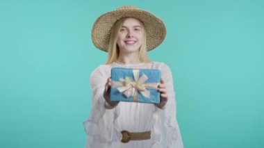 Mavi arka planda mutlu genç hippi kadın hediye kutusu. Genç kız gülümsüyor, kameraya hediye veriyor. Sana bir sürprizim var. Yüksek kalite 4k