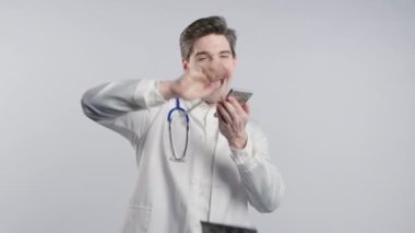 Zengin doktor para saçıyor. Beyaz önlüklü yakışıklı sağlık çalışanı Amerikan doları banknotlarını fazla harcadı. Beyaz stüdyo geçmişi. Yüksek kalite 4k görüntü