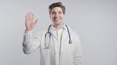 Dost canlısı Amerikan Olgun 30 'lu yaşlardaki beyaz önlüklü doktor el sallıyor. Beyaz stüdyoya selamlar. Yüksek kalite 4k görüntü