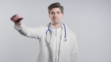 Mutsuz doktor portresi beyaz önlüklü adam sevmeme belirtileriyle kınanıyor. Olgun doktor, beyaz stüdyo arka planında olumsuz bir hareket göstererek memnuniyetsizliğini dile getiriyor..