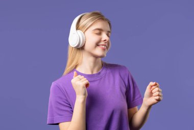 Mutlu kadın kafayı buluyor, müzik dinliyor, Violet stüdyo arka planında kulaklıklarla dans ediyor. Radyo, kablosuz modern ses teknolojisi, çevrimiçi çalar. Yüksek kalite